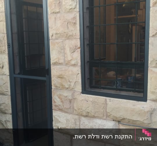 דלת וחלון אלומיניום עם סורגים על קיר אבן